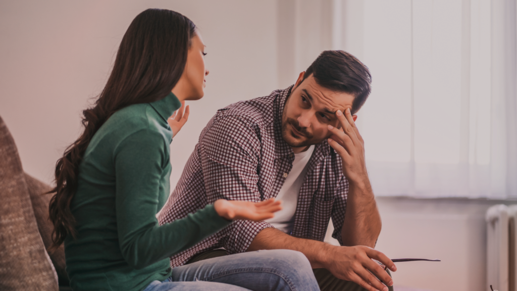 Casal conversando no sofá; a mulher parece explicar algo com intensidade emocional enquanto o homem escuta com expressão cansada e confusa, representando o desafio de tratar um relacionamento.