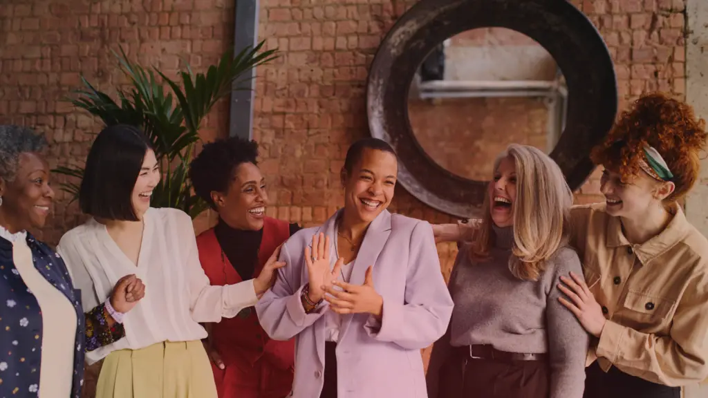 Grupo diverso de mulheres sorrindo e celebrando juntas em um ambiente descontraído. A imagem transmite conexão, alegria, sororidade e acolhimento entre mulheres inspiradoras de diferentes idades e origens.
