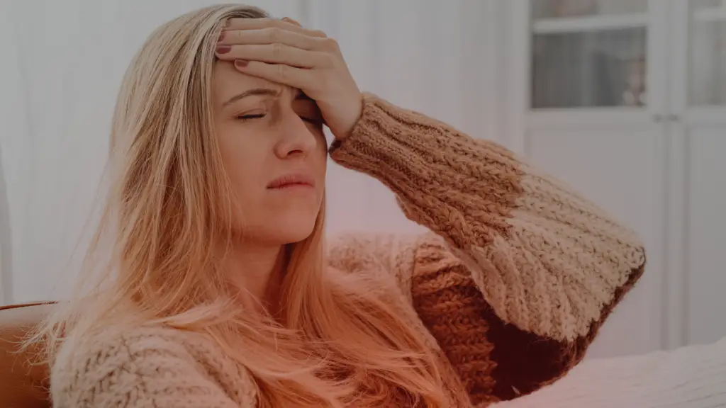 Mulher com expressão de sofrimento emocional, sentada e com a mão na testa, demonstrando angústia e confusão. A imagem representa o impacto emocional do término de um relacionamento e a dificuldade em se desligar do ex-parceiro.