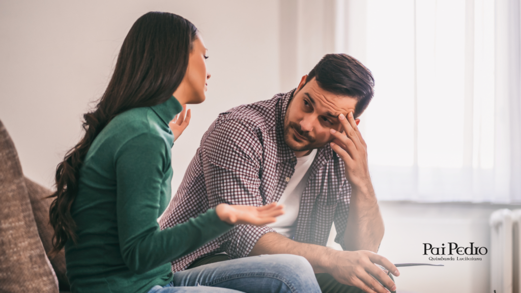 Casal sentado em um sofá, discutindo seriamente. A mulher gesticula enquanto o homem mantém a mão na testa em sinal de preocupação, representando um momento difícil na relação. O logotipo de Pai Pedro está presente no canto inferior direito, sugerindo um contexto de orientação espiritual para o término.