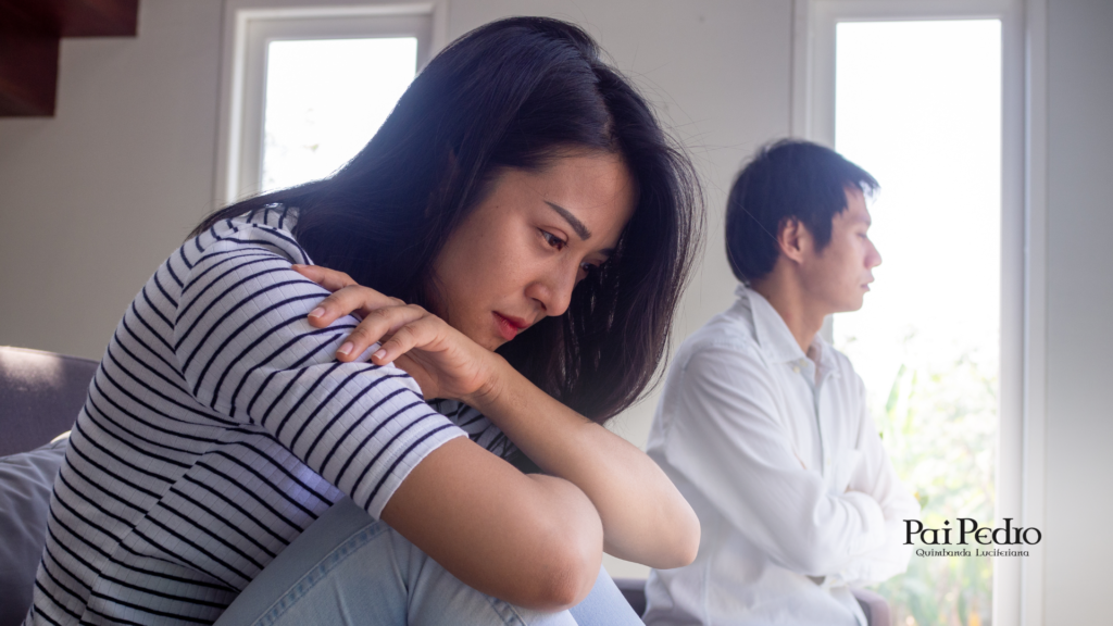 Mulher com expressão de tristeza e olhar distante enquanto um homem permanece de costas em segundo plano. A imagem retrata um momento de silêncio e desconexão emocional, simbolizando uma relação em crise. No canto inferior direito, o logotipo de Pai Pedro, sugerindo a busca por orientação espiritual em momentos de término.