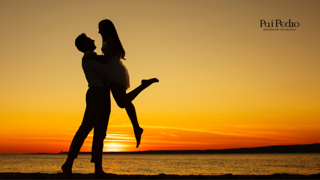Casal se abraçando e sorrindo à beira-mar durante o pôr do sol, com o céu em tons dourados e alaranjados. A silhueta dos dois reflete afeto, leveza e esperança, simbolizando como namorar. 