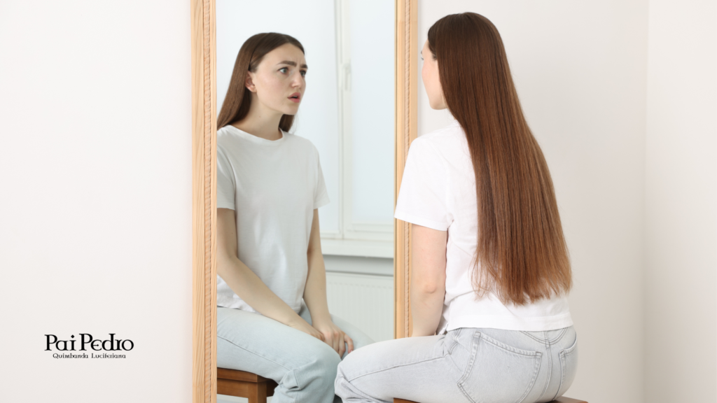 Mulher sentada diante do espelho, olhando para o próprio reflexo com expressão de incerteza, simbolizando o processo de autoconhecimento e reconstrução após a prisão afetiva.