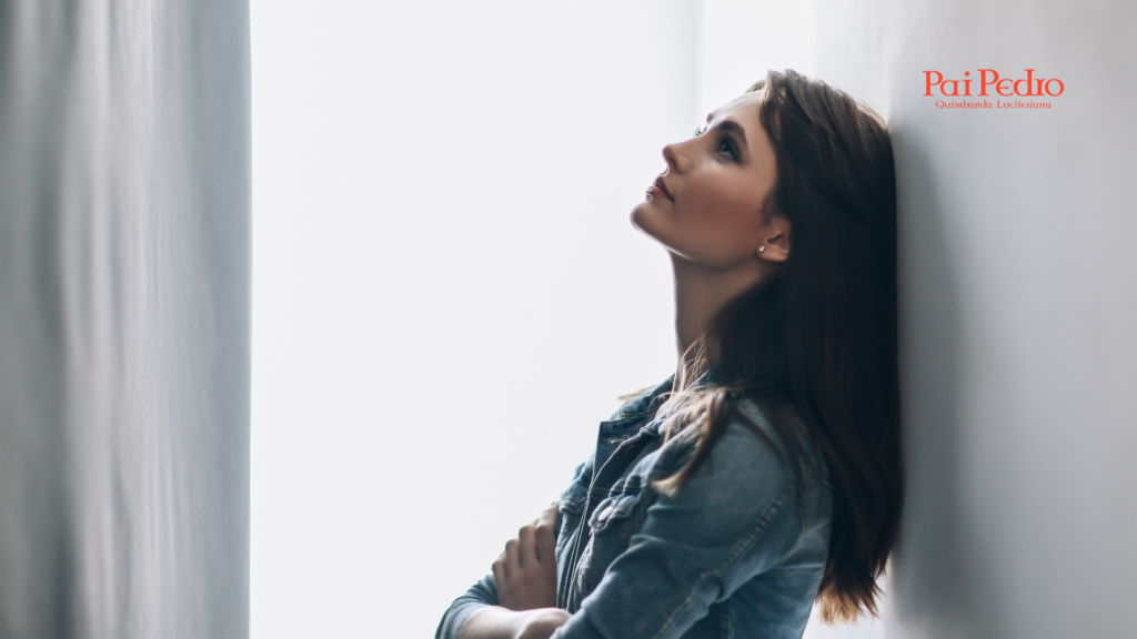 Mulher encostada em uma parede clara, com expressão pensativa e olhar voltado para cima. A iluminação suave cria uma atmosfera introspectiva e emocional, simbolizando pausa, reflexão e autoconhecimento diante de um término ou decisão amorosa.