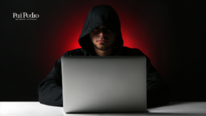 Pessoa usando um moletom com capuz preto, parcialmente iluminada pela luz vermelha ao fundo, digitando em um notebook prateado sobre uma mesa. A cena transmite mistério e tensão, remetendo à investigação e exposição de um tema sensível relacionado à fé, estelionato religioso e manipulação.