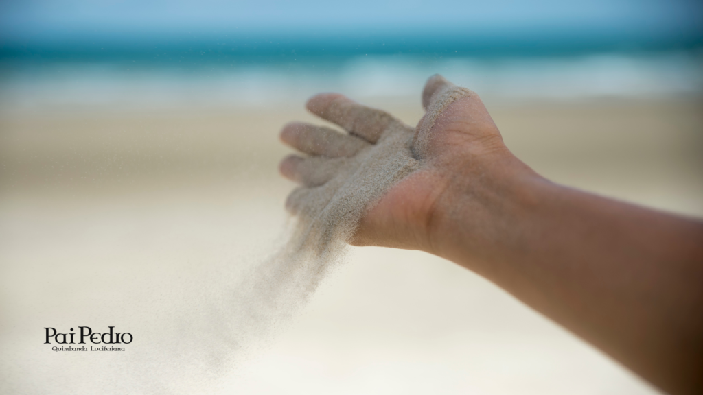 Mão deixando a areia escorrer na praia, representando o ato de desapegar de alguém como um processo consciente de soltar o que não se sustenta mais e recuperar equilíbrio emocional.