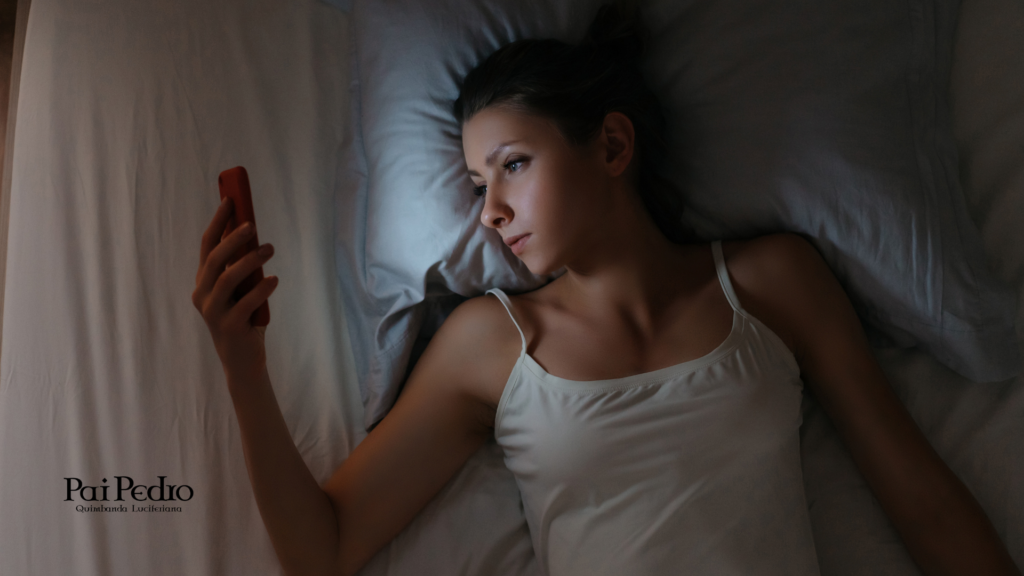 Mulher deitada na cama durante a noite olhando fixamente para o smartphone, ilustrando o vício em celular e o impacto da dependência digital no sono e na saúde mental.