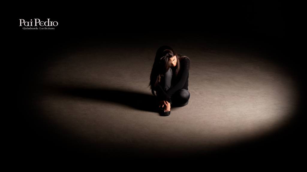 Mulher sentada sozinha sob uma luz dramática em ambiente escuro, representando baixa autoestima, dor emocional, insegurança e isolamento interior.