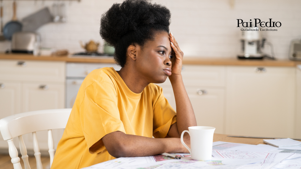 Mulher sentada à mesa com expressão cansada e mão na cabeça, representando exaustão emocional, sobrecarga mental e desgaste psicológico no dia a dia.
